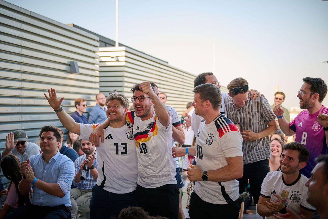 Gruppe von Fußballfans auf einer Dachterrasse, die in deutschen Trikots jubeln und feiern; im Hintergrund weitere Zuschauer, die das Spiel verfolgen.