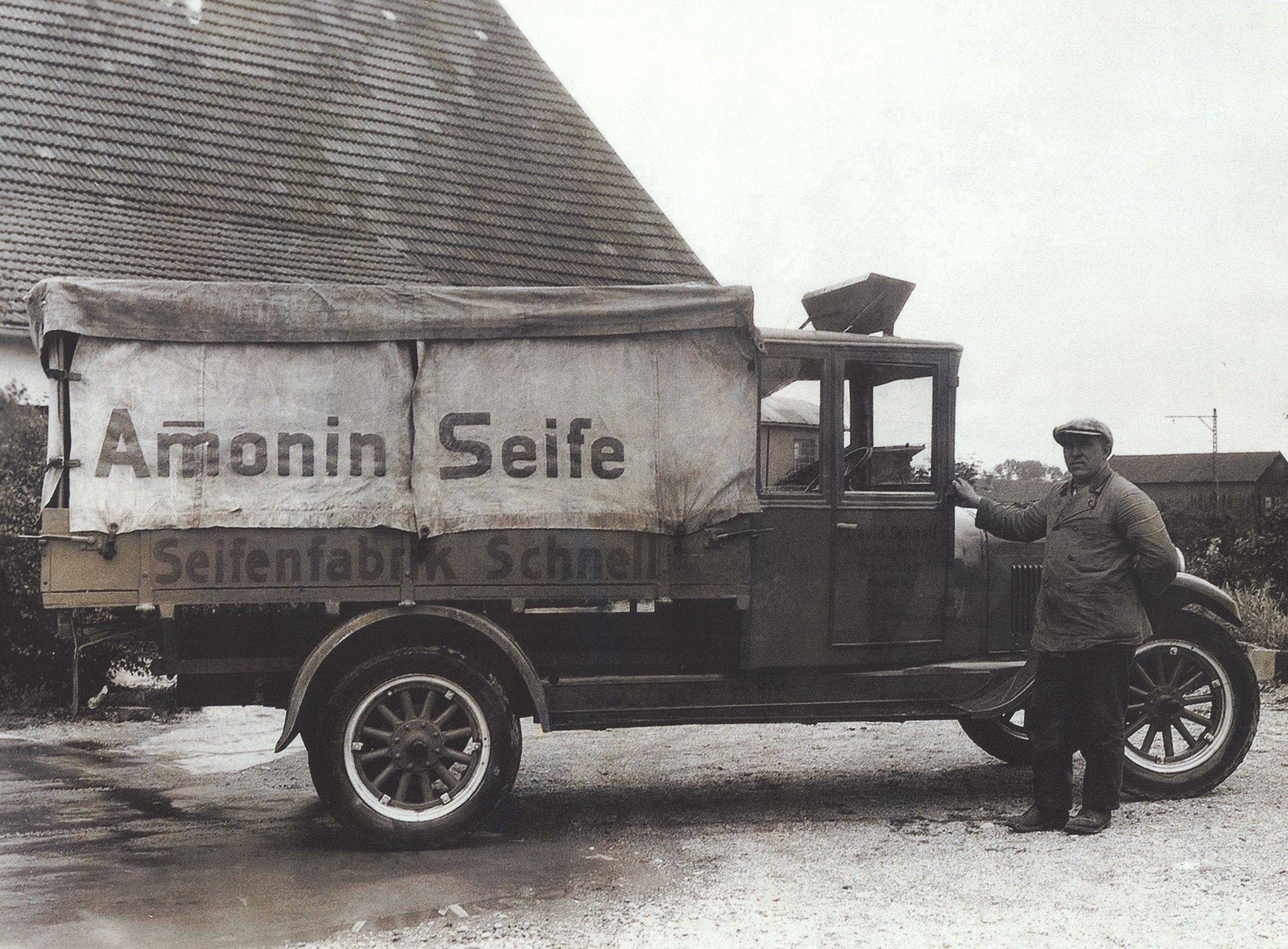 Historisches Foto eines Lieferwagens der Seifenfabrik Schnell mit der Aufschrift "Amonin Seife" und einem Fahrer, der neben dem Fahrzeug steht.