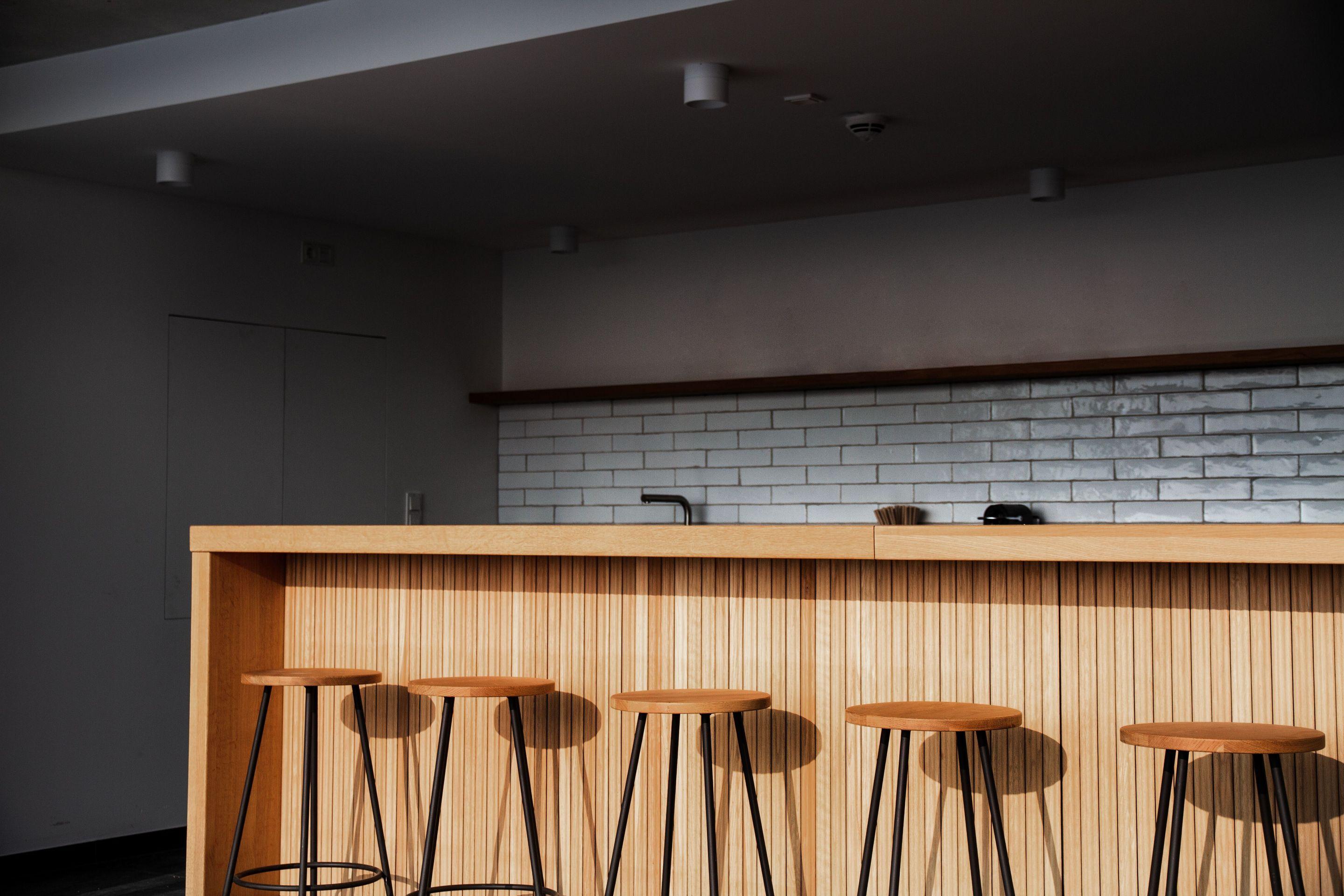 Minimalistisch gestalteter Gastronomiebereich in der Neuen Siederei mit einer hölzernen Theke, Barhockern und einer weißen Kachelwand im Hintergrund.